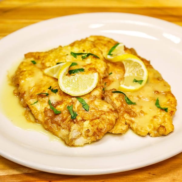 Golden pan-fried fish fillets garnished with lemon slices and parsley on a white plate.