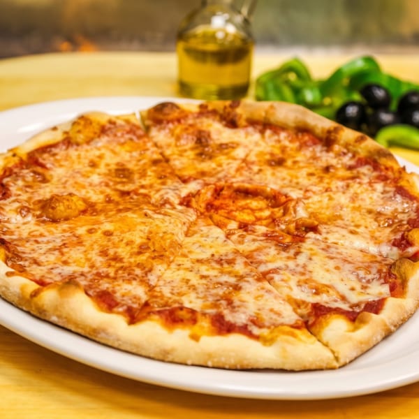 Cheesy pepperoni pizza on a white plate, served with green peppers, black olives, and a beverage on a wooden table.