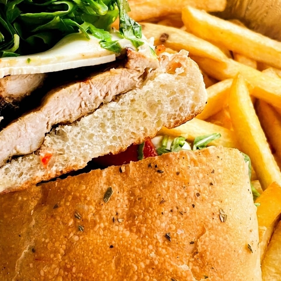 Close-up of a chicken sandwich with mozzarella, arugula, and fries in a foil container.