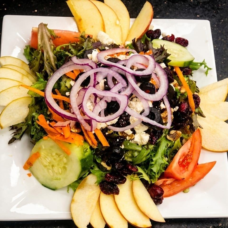 Fresh garden salad with mixed greens, red onions, apples, cucumbers, tomatoes, and cranberries.
