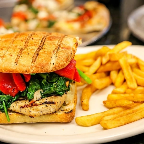 Grilled chicken panini with roasted red peppers and spinach, served with a side of french fries.