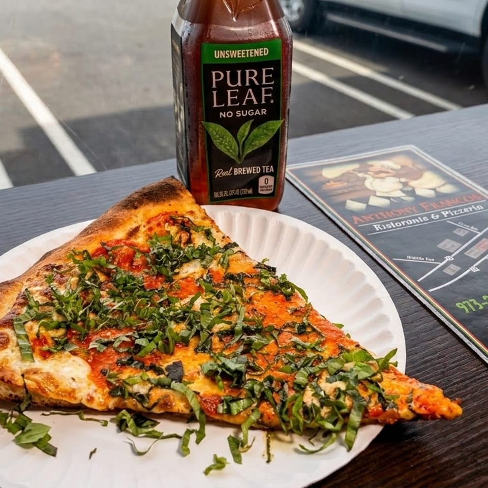 A slice of pizza with basil and a Pure Leaf iced tea bottle on a table with a menu.