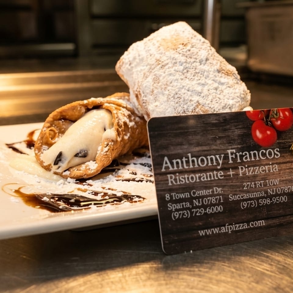 Two cannolis dusted with powdered sugar and chocolate syrup, with an Anthony Francos business card.