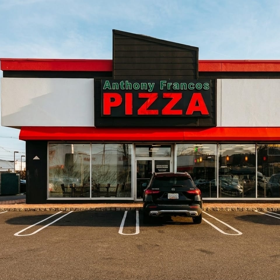 Exterior of Anthony Franco's Pizza restaurant with a red and black sign, parking lot, and cars.