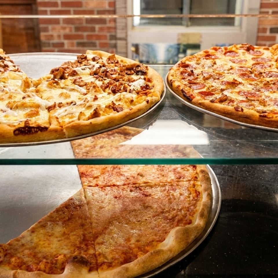 Three large pizzas, two whole and one with a slice removed, displayed in a glass case.