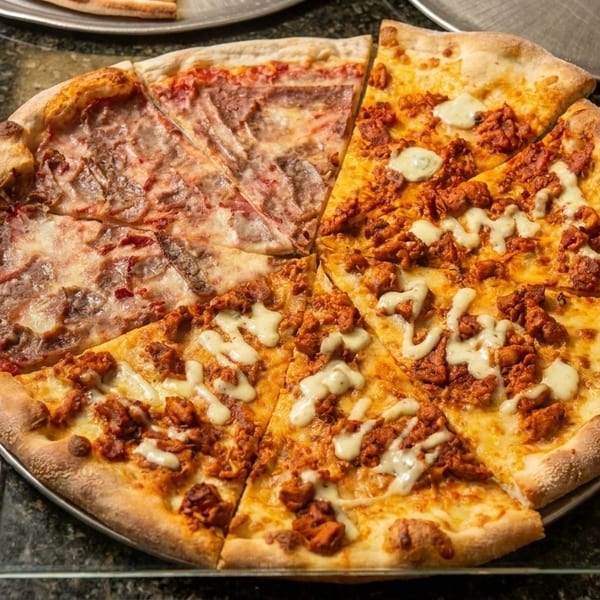 Half pepperoni and half chicken pizza with white sauce, on a metal tray.